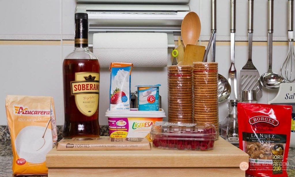 Los ingredientes de la tarta sobre la encimera: galletas maría doradas, brandy, azúcar, nata, yogur natural, chocolate de fundir, nueces y frutos rojos