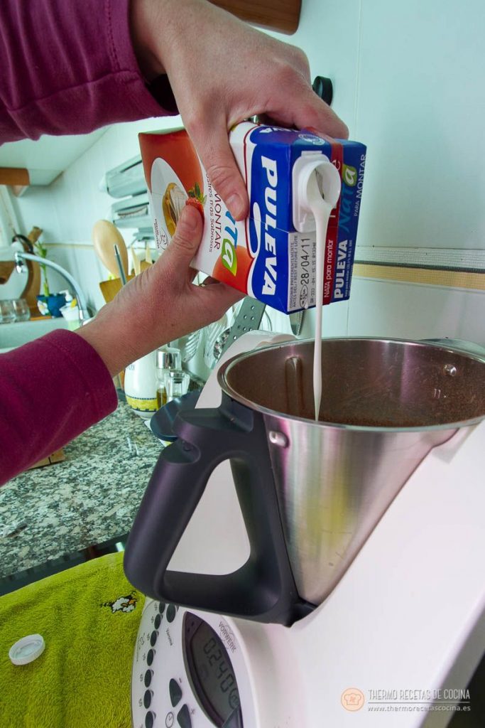 Nata para montar vertiéndose desde el brik sobre el chocolate negro ya triturado en el vaso
