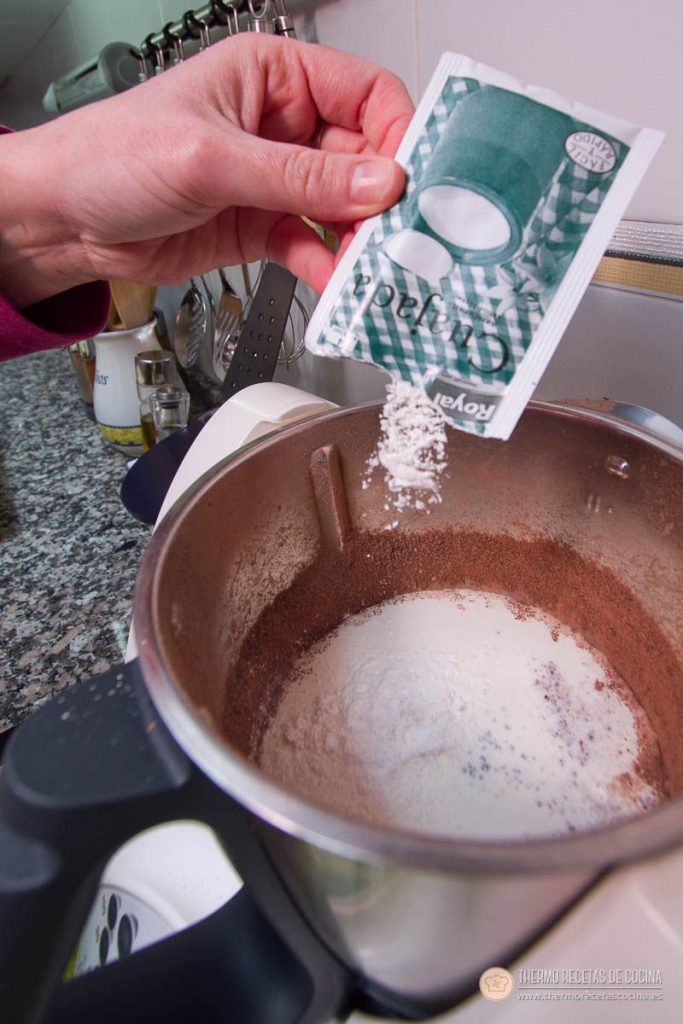 Sobre de cuajada en polvo cayendo en el vaso, sobre el chocolate triturado, el azúcar y los líquidos
