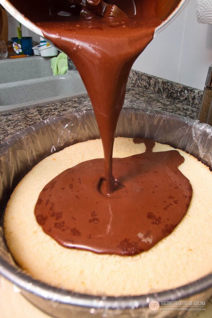 Crema de chocolate negro cayendo desde el vaso sobre la plancha de bizcocho, en un molde forrado con film