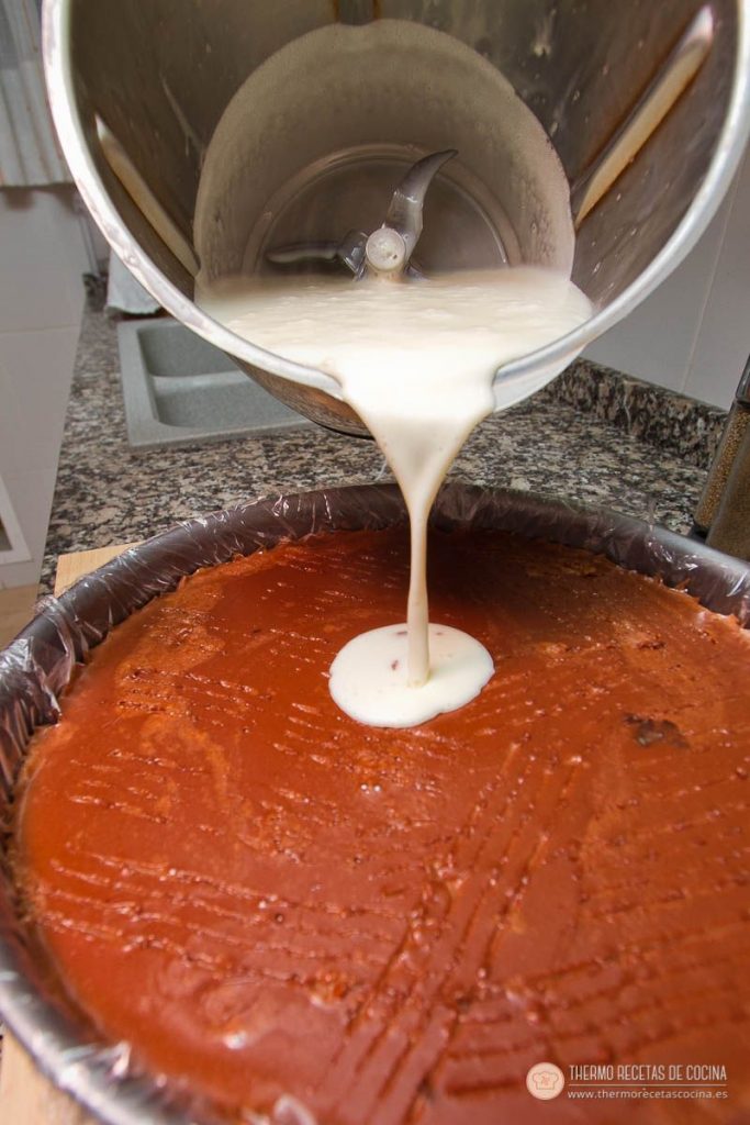 Crema de chocolate blanco cayendo sobre la capa de chocolate con leche, que está rayada con el tenedor
