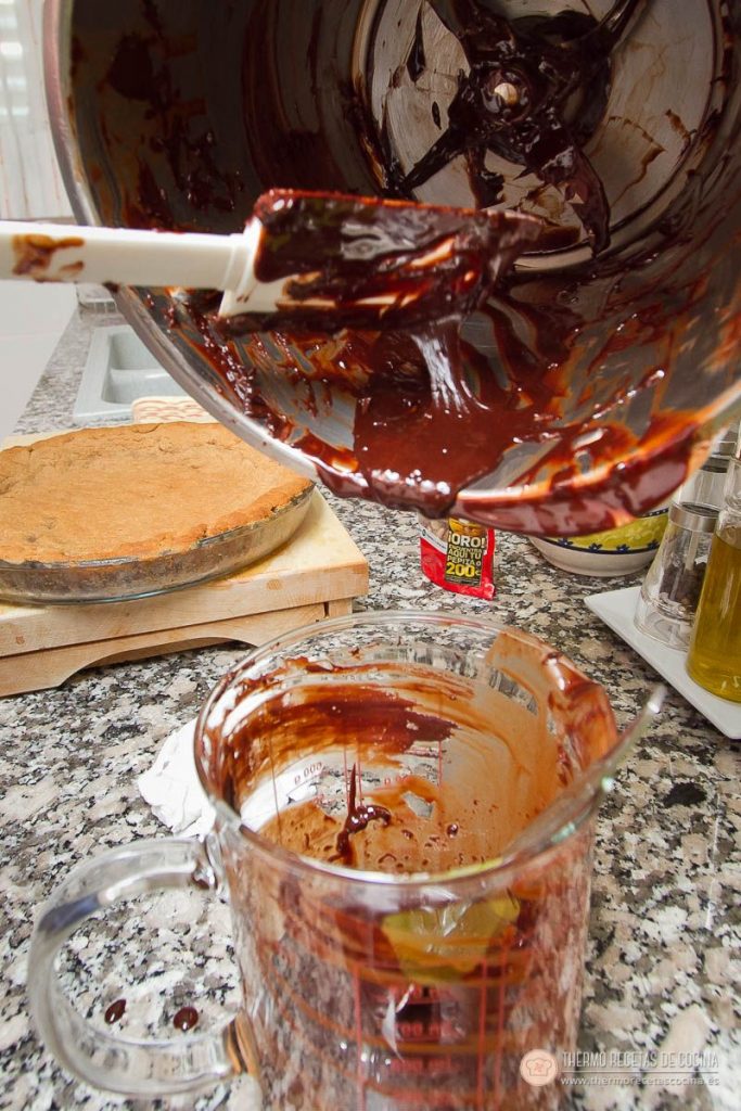 Chocolate fundido con brandy pasándose del vaso a una jarra, con la base de galleta ya horneada y dorada al lado