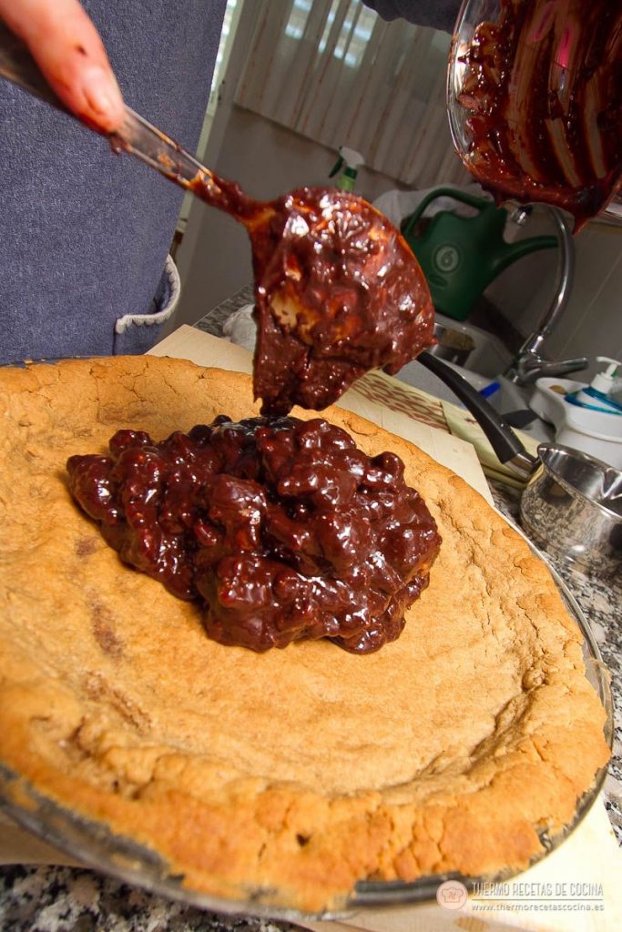 Cucharada de chocolate con nueces caramelizadas cayendo sobre la base de galleta recién horneada