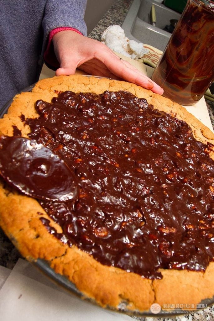 Cobertura de chocolate y nueces ya extendida sobre toda la base de galleta, hasta el borde