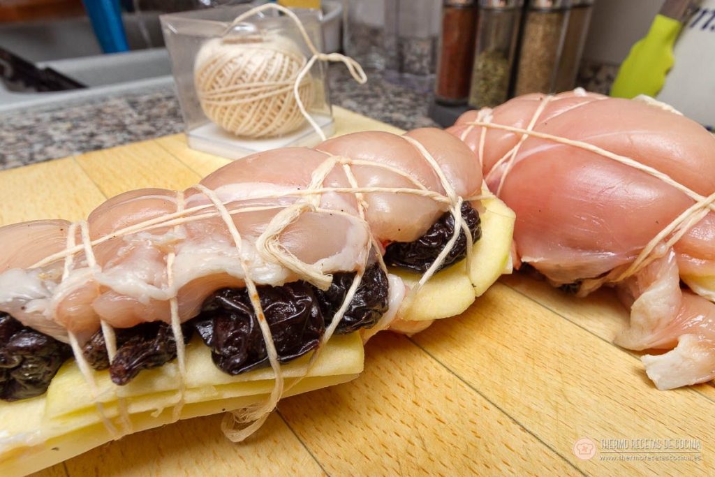 Los dos rollos de pechuga rellena atados con bramante sobre la tabla, con el ovillo de hilo detrás