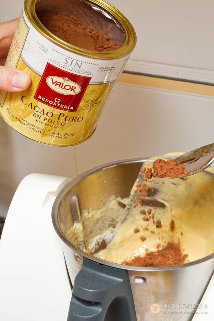 Plum-cake veteado | 10 | Thermo Recetas Cocina Lata de cacao puro llenando una cucharada sobre el vaso, con el cacao ya cayendo encima de la masa