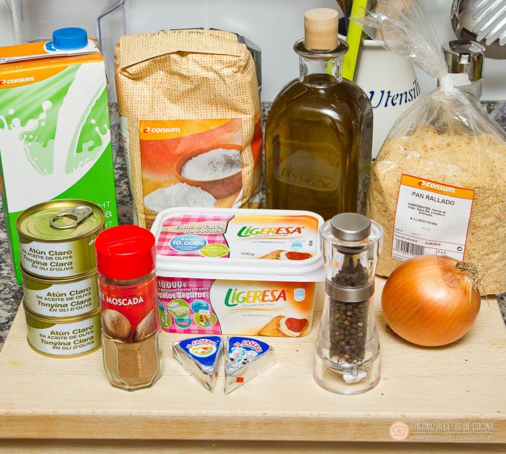 los ingredientes de las croquetas de atún sobre la encimera: tres latas de atún claro en aceite de oliva, harina, leche, aceite de oliva, dos tarrinas de margarina, dos quesitos, nuez moscada, molinillo de pimienta, una cebolla y pan rallado
