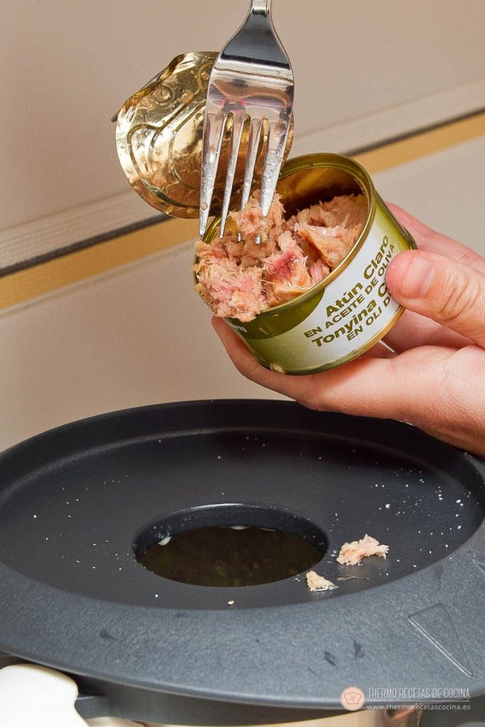 añadiendo el atún de la lata con un tenedor por el bocal del vaso