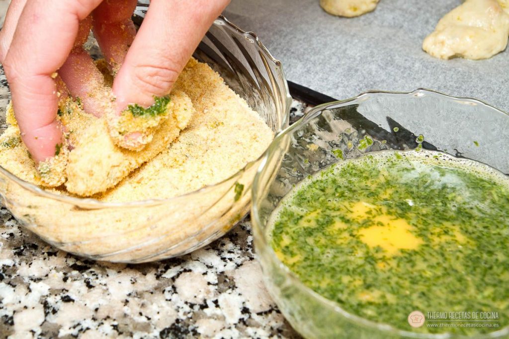 croquetas rebozándose en un bol de pan rallado, junto al bol de huevo batido con perejil