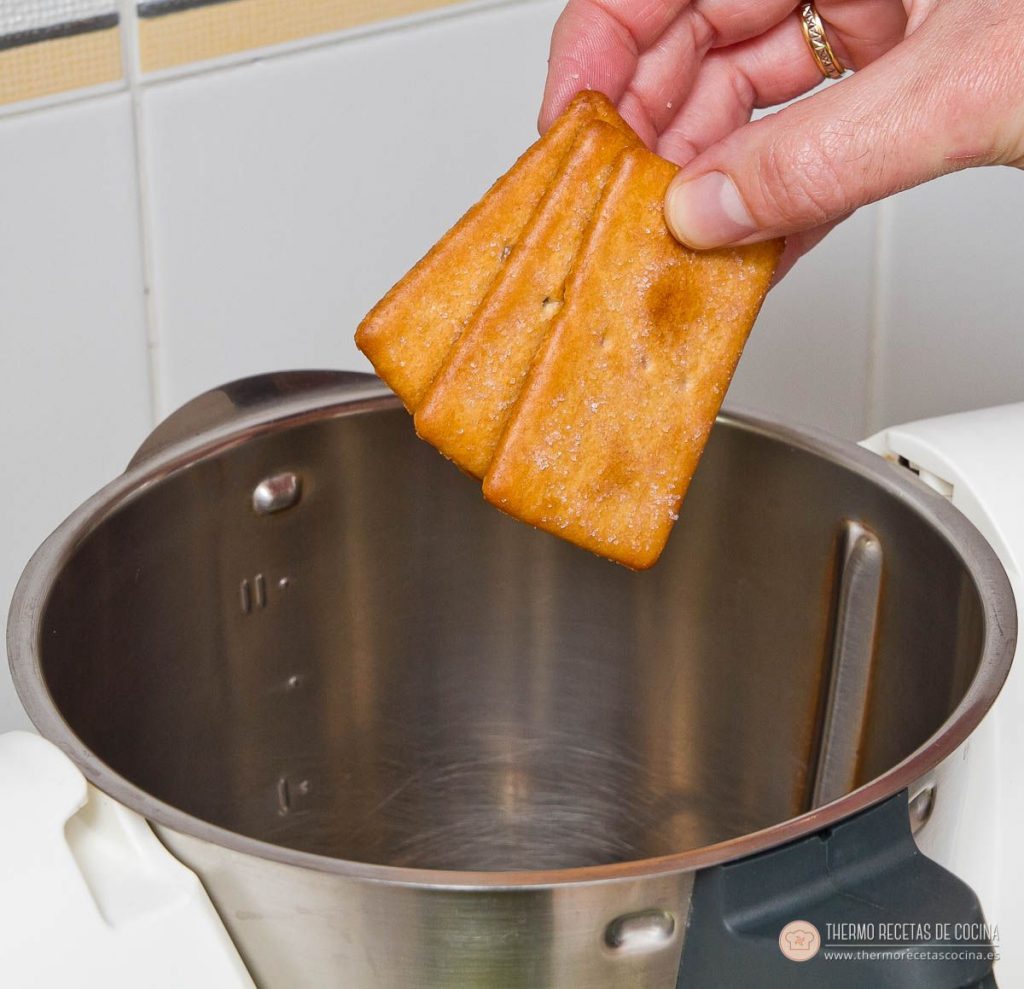 Natillas de napolitana | 4 | Recetas de cocina para Thermomix mano dejando caer las galletas napolitanas dentro del vaso de la Thermomix antes de triturarlas
