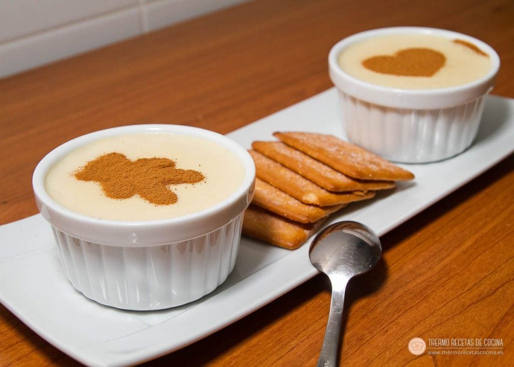 Natillas de napolitana | 2 | Recetas de cocina para Thermomix dos natillas de napolitana en cuencos individuales, con canela espolvoreada dibujando un osito y un corazón, y galletas napolitanas de acompañamiento