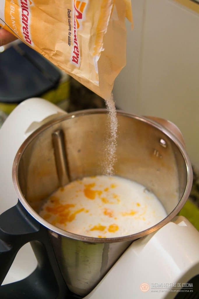 Azúcar cayendo desde el paquete sobre la mezcla de leche y huevo del vaso, con las motas amarillas de la yema todavía sin integrar