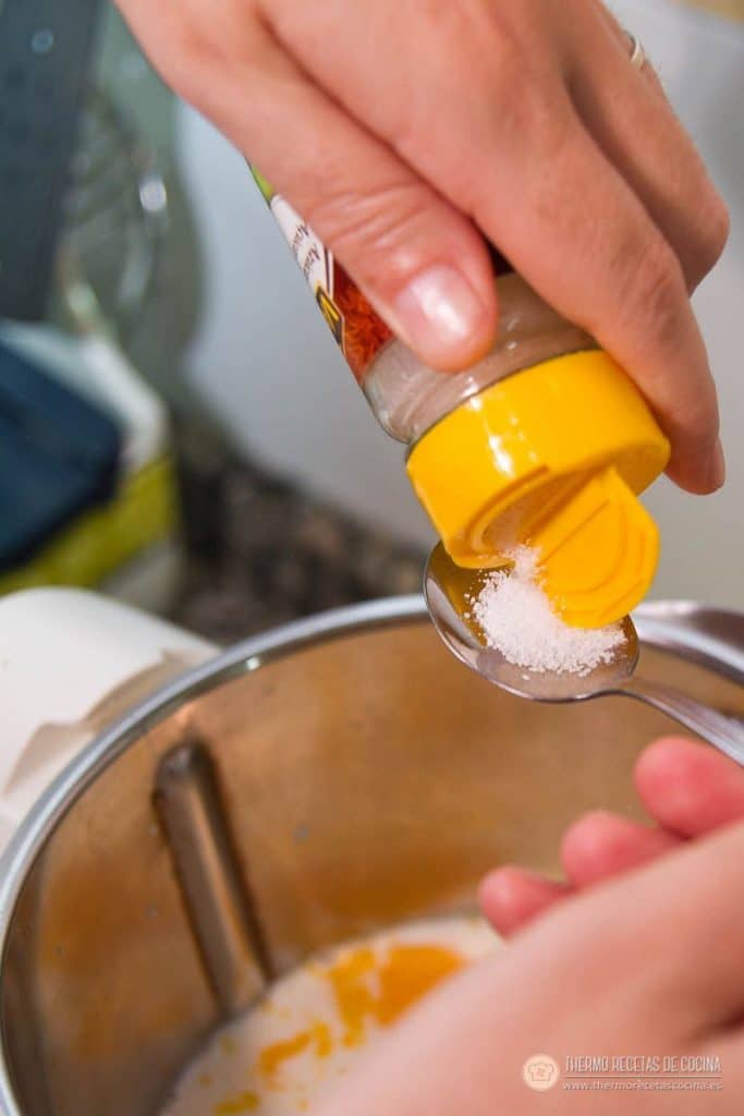 Añadiendo una cucharada de azúcar avainillado desde el botecito al vaso con la mezcla del flan