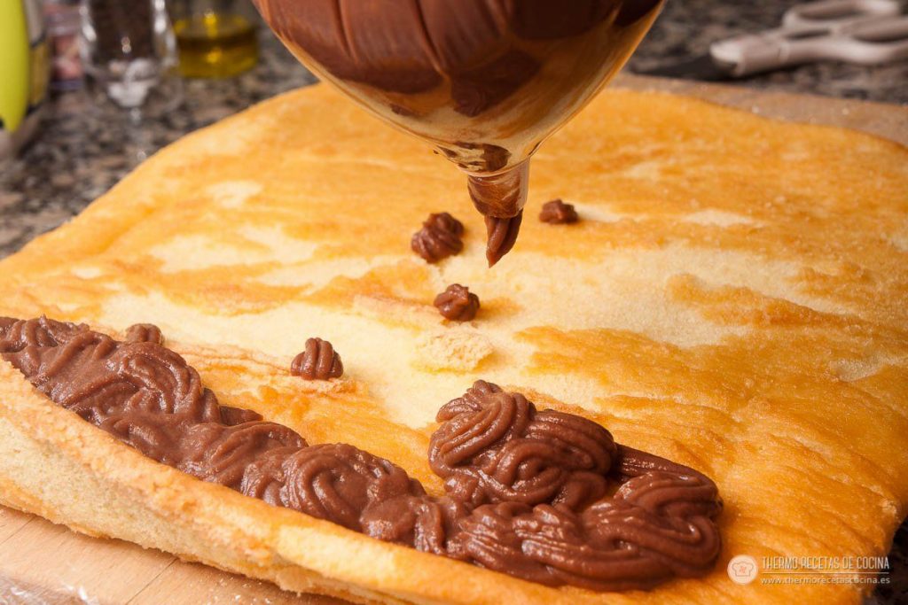 manga pastelera depositando la crema de trufa de chocolate en una tira gruesa sobre el borde del bizcocho extendido