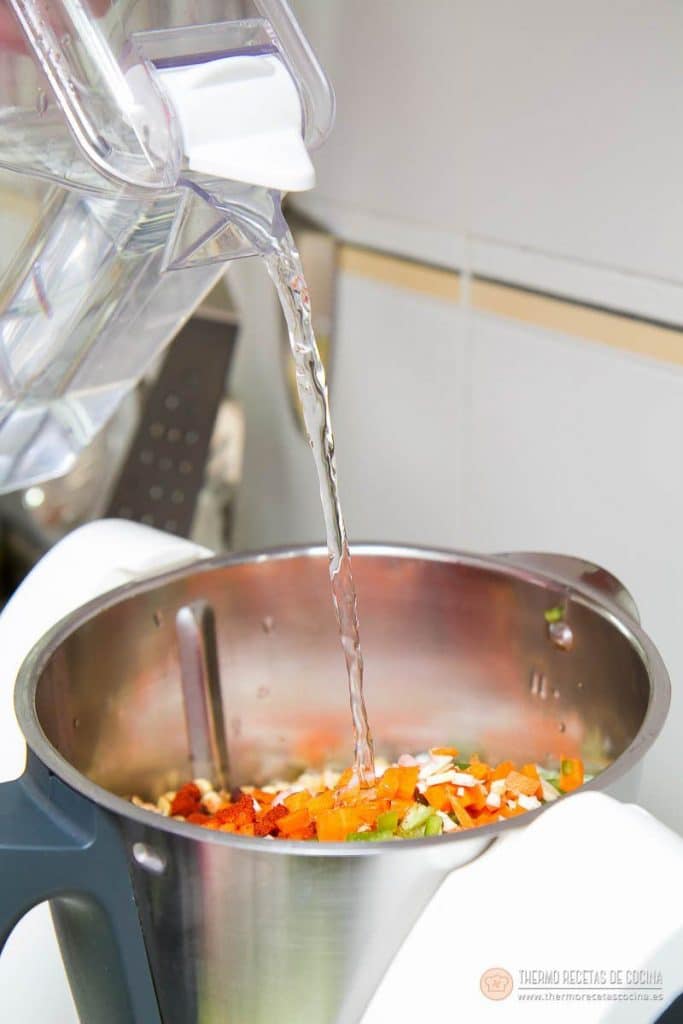 Vertiendo el agua de la jarra en el vaso de la Thermomix, sobre las lentejas, la verdura y el pimentón