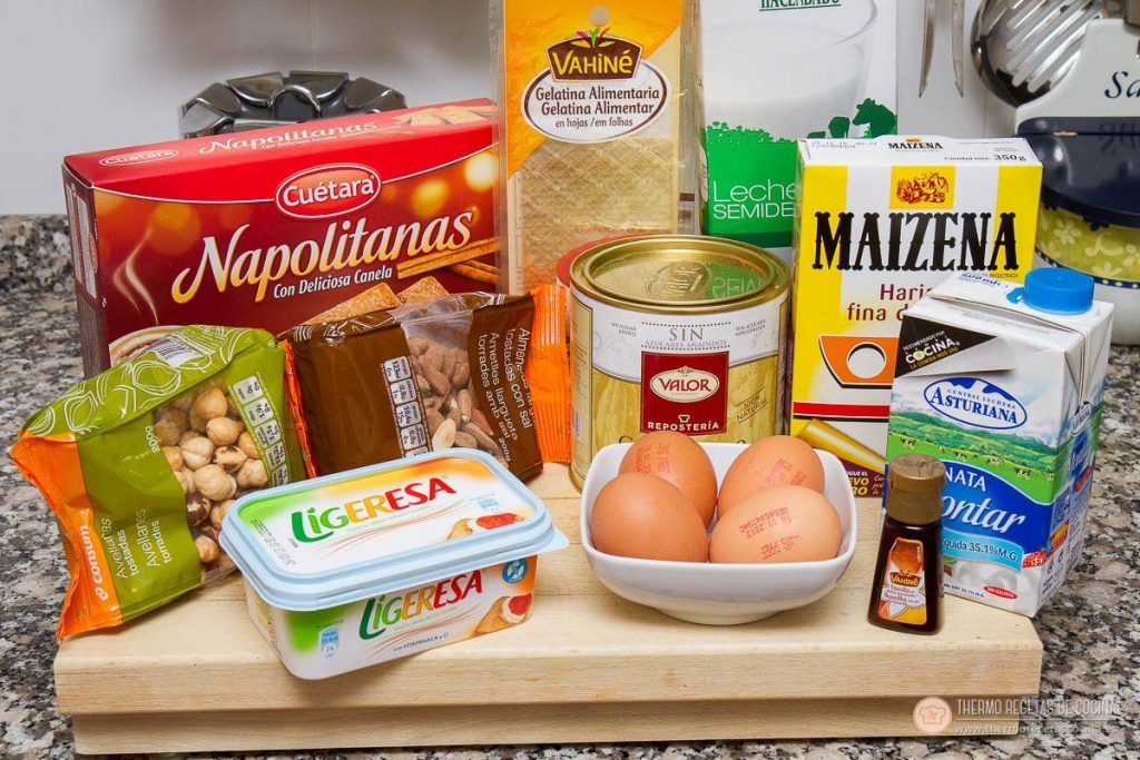 Los ingredientes sobre la tabla: paquete de galletas napolitanas de canela, gelatina en hojas, avellanas y almendras tostadas, cacao puro de repostería, huevos, harina fina de maíz, leche, nata para montar y vainilla líquida