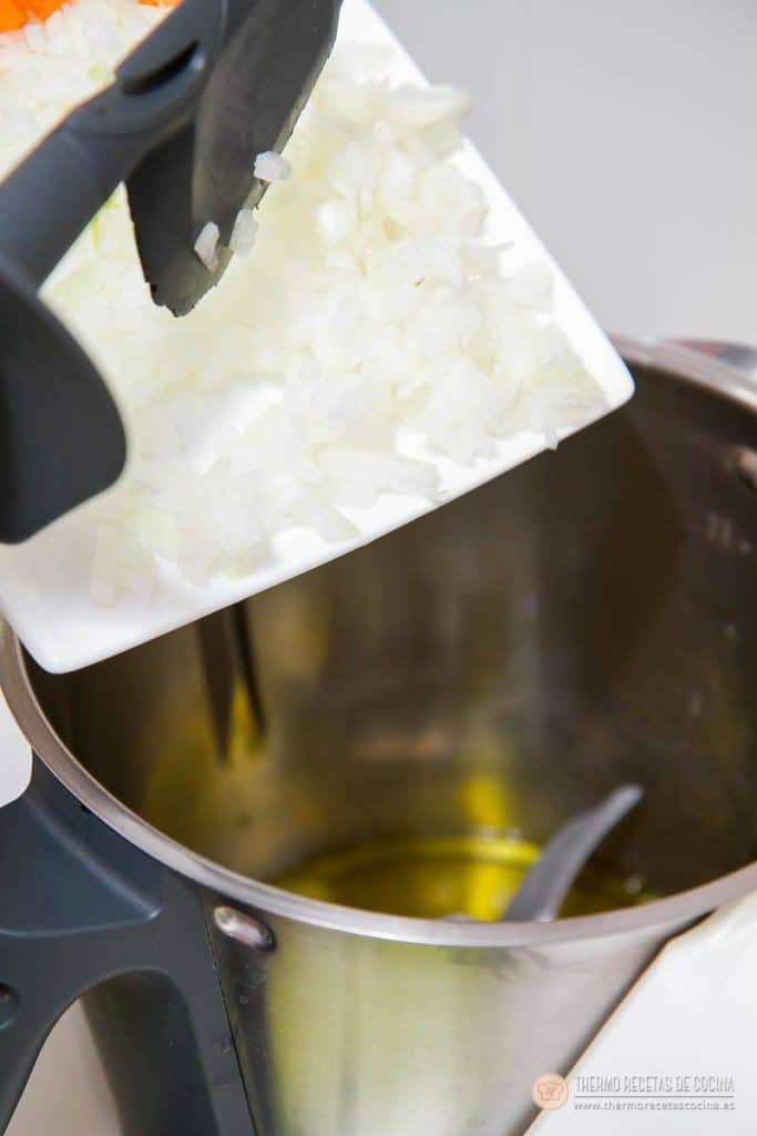 Cebolla troceada cayendo dentro del vaso de la Thermomix con el aceite ya caliente