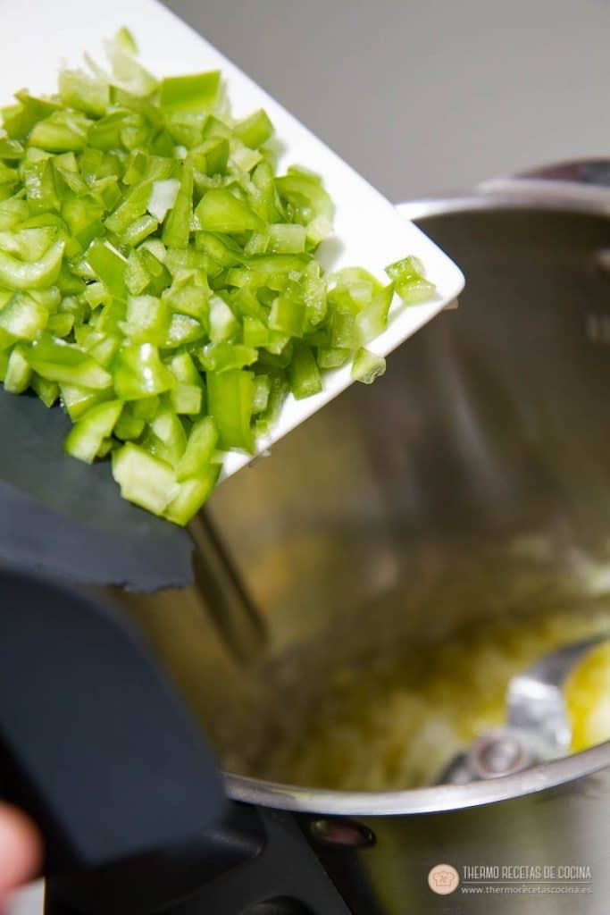 Pimiento verde troceado añadiéndose al vaso sobre la cebolla ya pochándose