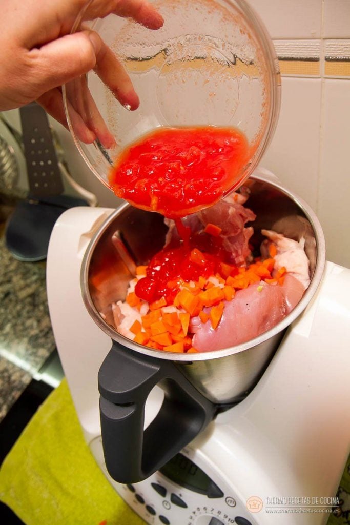 Tomate natural triturado vertiéndose sobre el pollo, la zanahoria y el sofrito en el vaso