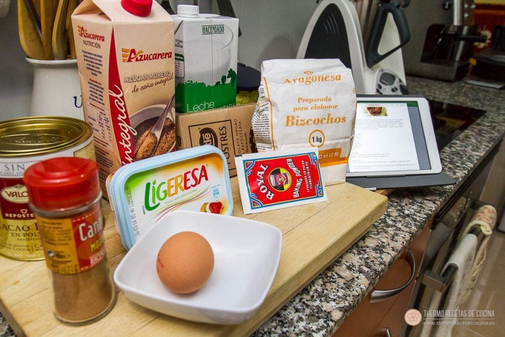 Bizcocho Chocolate y Canela | 3 | Thermo Recetas Cocina Ingredientes del bizcocho de chocolate y canela sobre la encimera: cacao en polvo, bote de canela, azúcar moreno, leche, harina, levadura, una tarrina de margarina ligera y un huevo