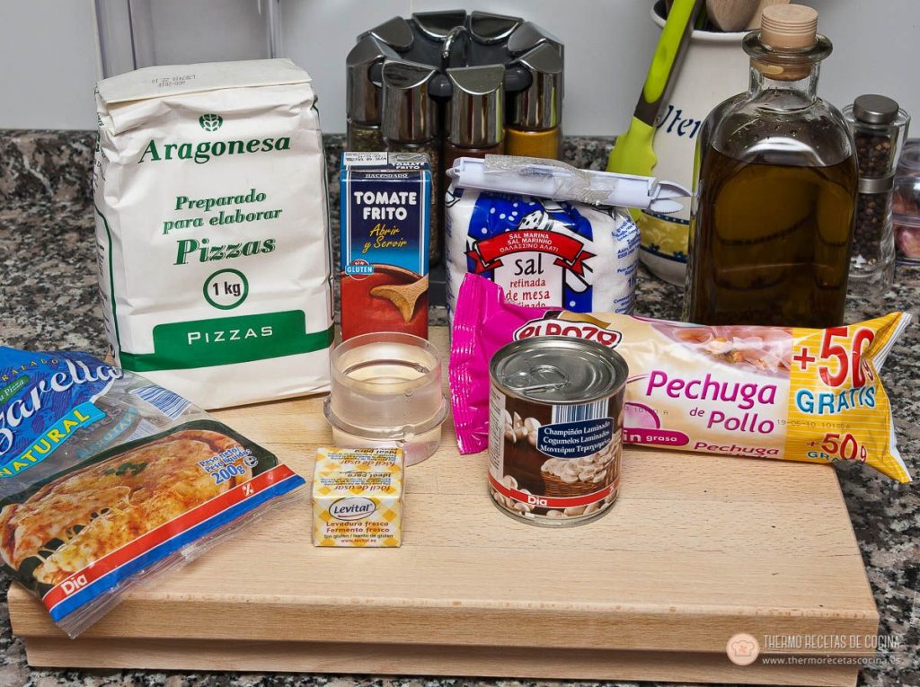 Todo lo necesario sobre la encimera: preparado de harina para pizzas, levadura fresca en pastilla, aceite, sal, tomate frito, lata de champiñones laminados, pechuga en fiambre y mozzarella rallada