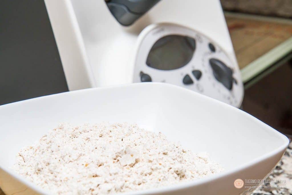harina de espelta integral con sus motas de salvado en un bol blanco, delante del vaso de la Thermomix