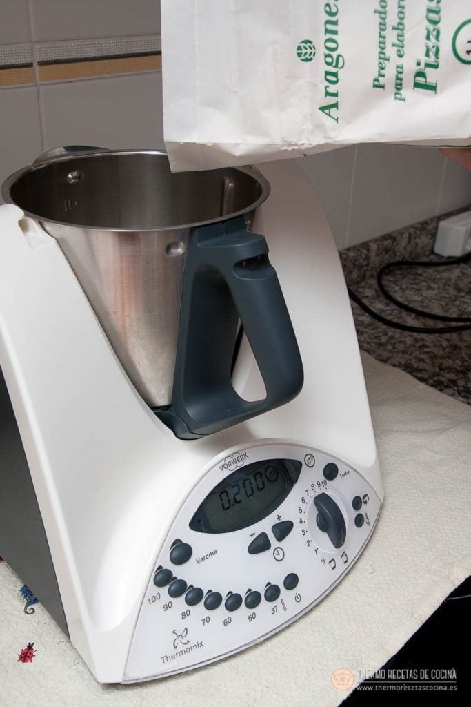 Vertiendo el preparado de harina para pizzas en el vaso de la Thermomix, con la báscula en marcha
