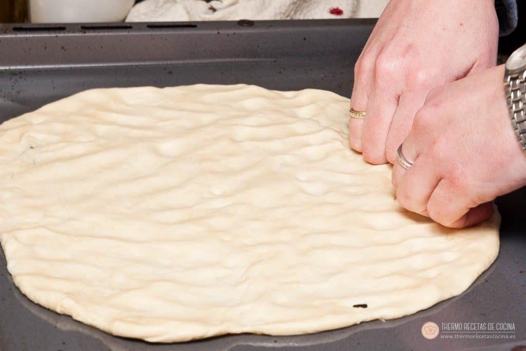 Estirando la masa de pizza con las manos, ya fina y redonda, sobre la bandeja del horno