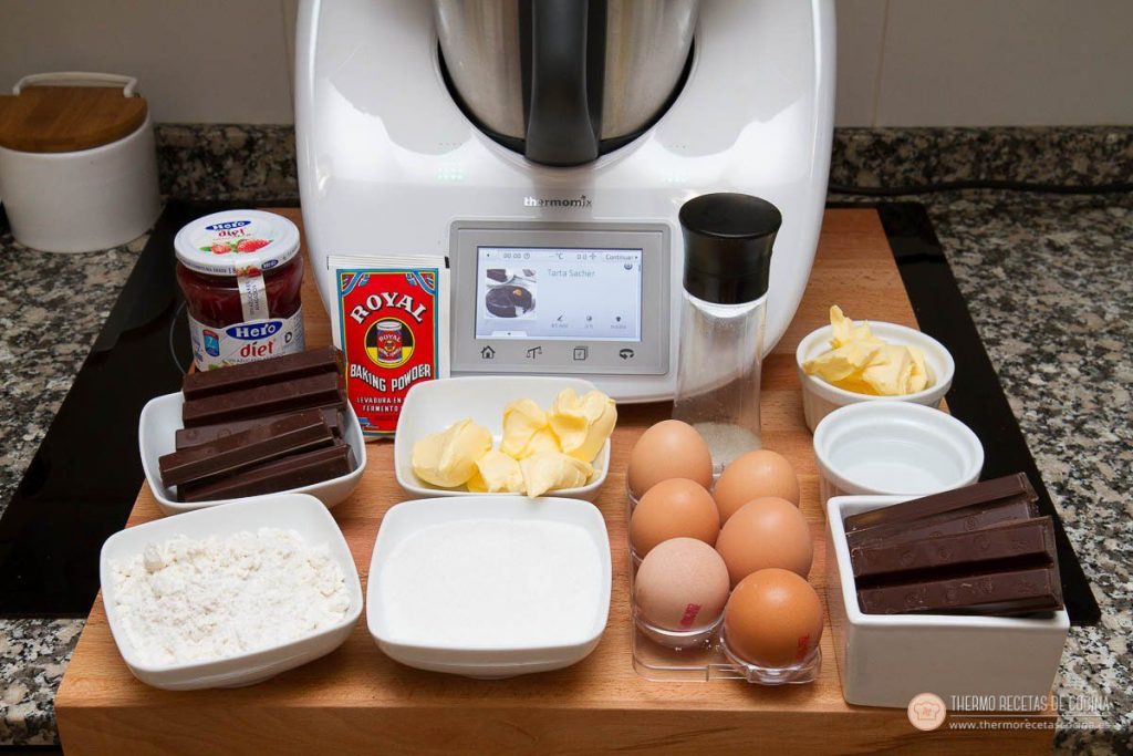 Todos los ingredientes pesados delante de la Thermomix: dos tandas de chocolate fondant, mantequilla, huevos, harina, azúcar, agua, levadura química y el bote de mermelada de fresa