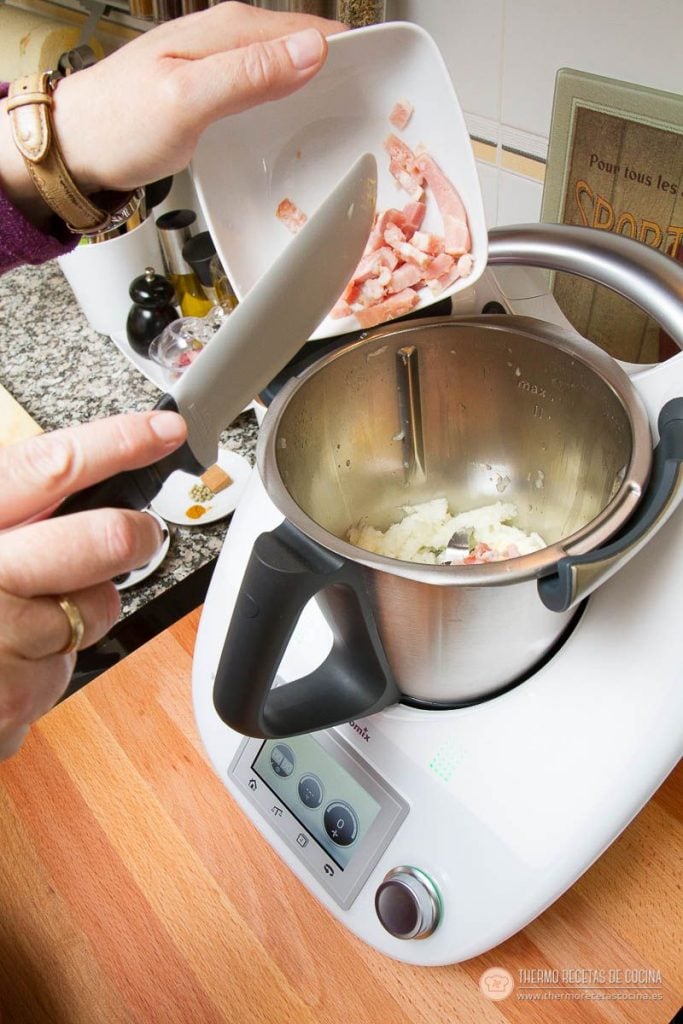 Dados de beicon añadiéndose al vaso sobre la cebolla y la mantequilla