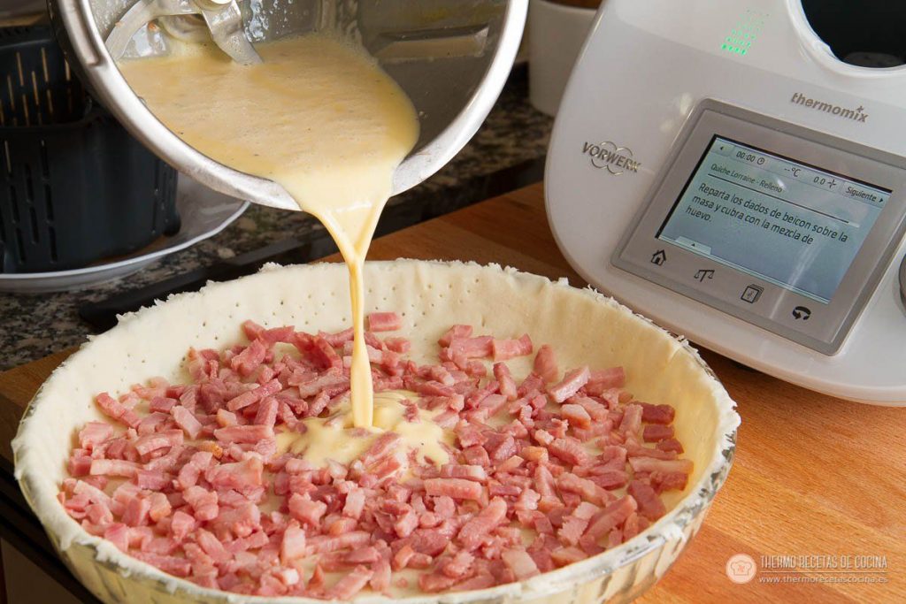 Receta de tarta Quiché de Bacon y Queso | 6 | Recetas de cocina para Thermomix la mezcla de huevo y nata cayendo sobre el bacon repartido en la base de masa quebrada