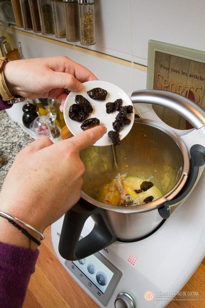Ciruelas pasas cayendo desde un platito sobre el sofrito de cebolla y beicon del vaso