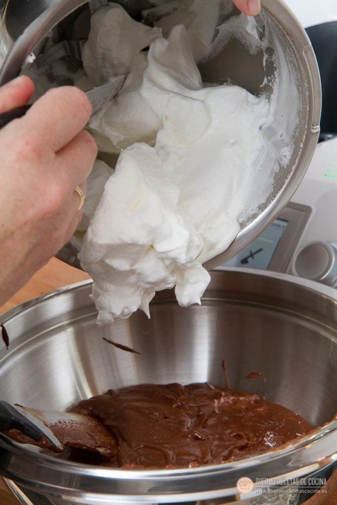 Merengue blanco y montado cayendo desde el vaso sobre la masa de chocolate reservada en un bol