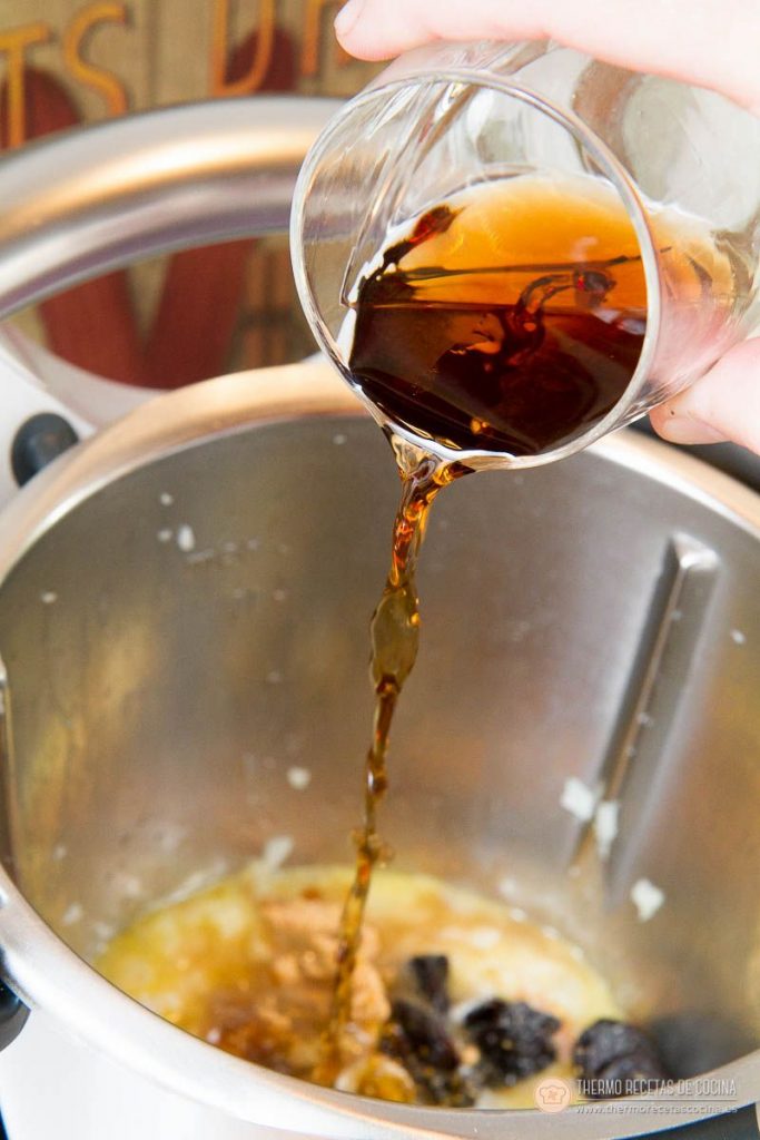 Vermut rojo vertiéndose dentro del vaso sobre el sofrito de cebolla, beicon, pasas y ciruelas