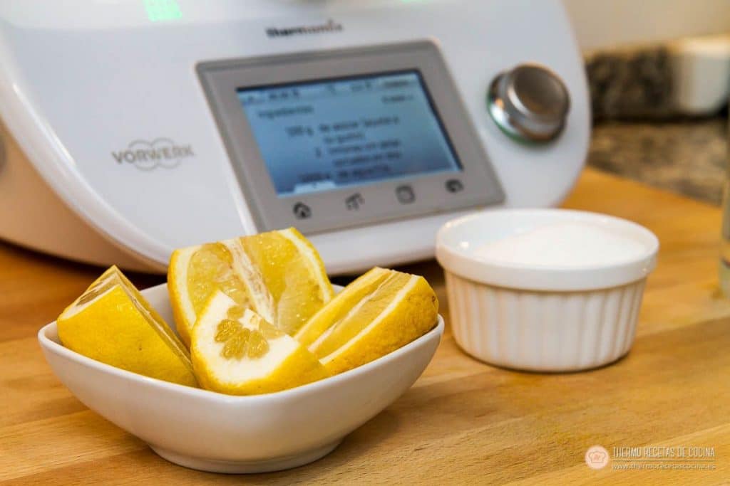 cuenco de limones cortados y ramequín de azúcar sobre la tabla de madera, delante de la Thermomix con la receta en pantalla