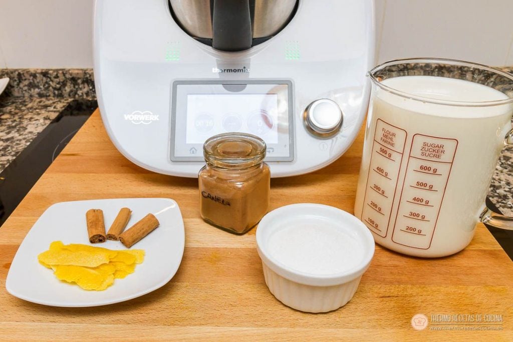 ¿Tardes de calor? Prepara una Leche Merengada con tu Thermomix. | 3 | Recetas de cocina para Thermomix piel de limón, canela en rama, un bote de canela molida, un cuenco de azúcar y una jarra de leche delante de la Thermomix