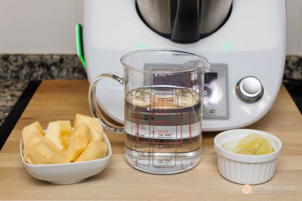 manzana pelada en trozos, limón pelado sin la parte blanca y una jarra medidora con agua fría junto a la Thermomix